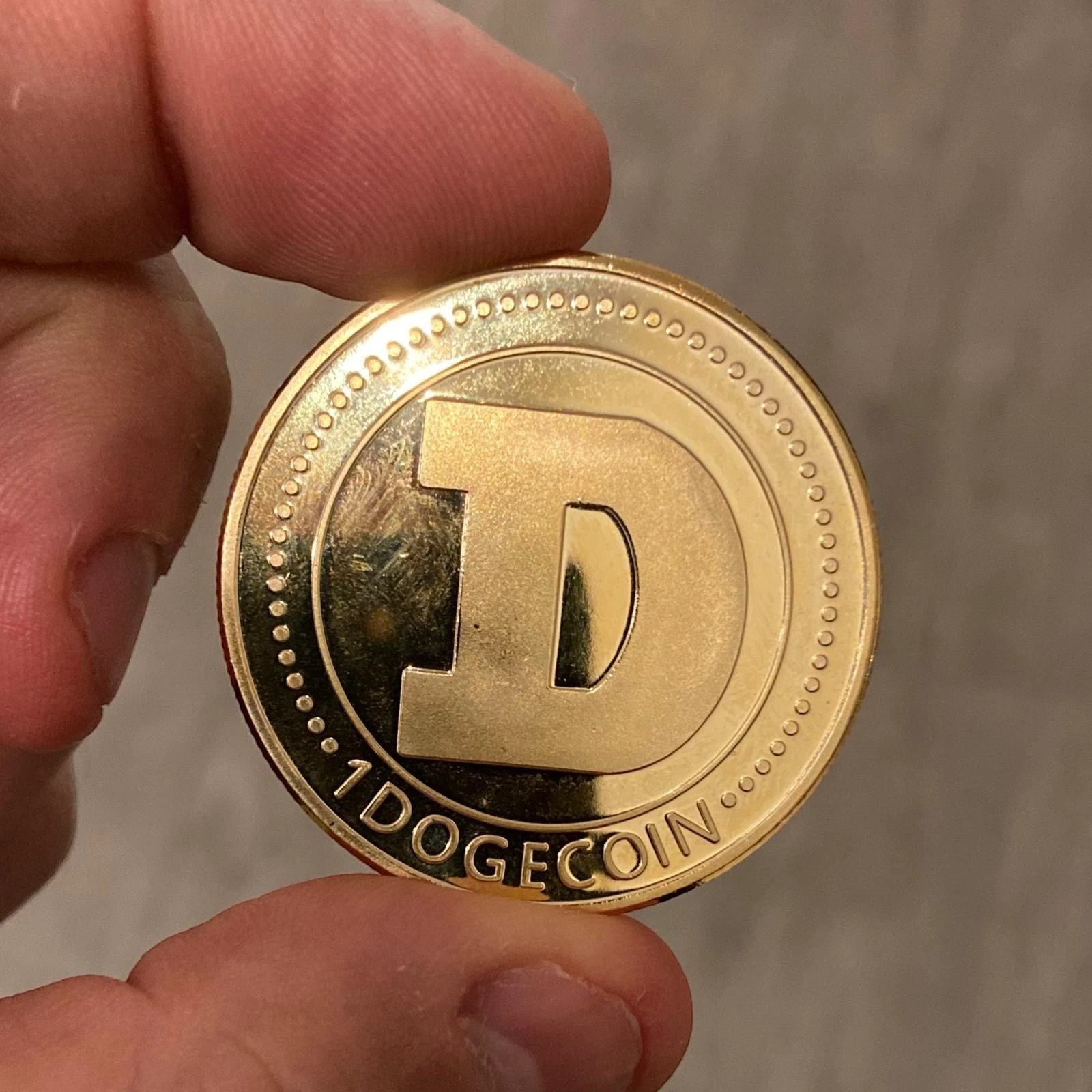 Back of the gold Dogecoin collectible coin showing the 1 DOGECOIN D logo