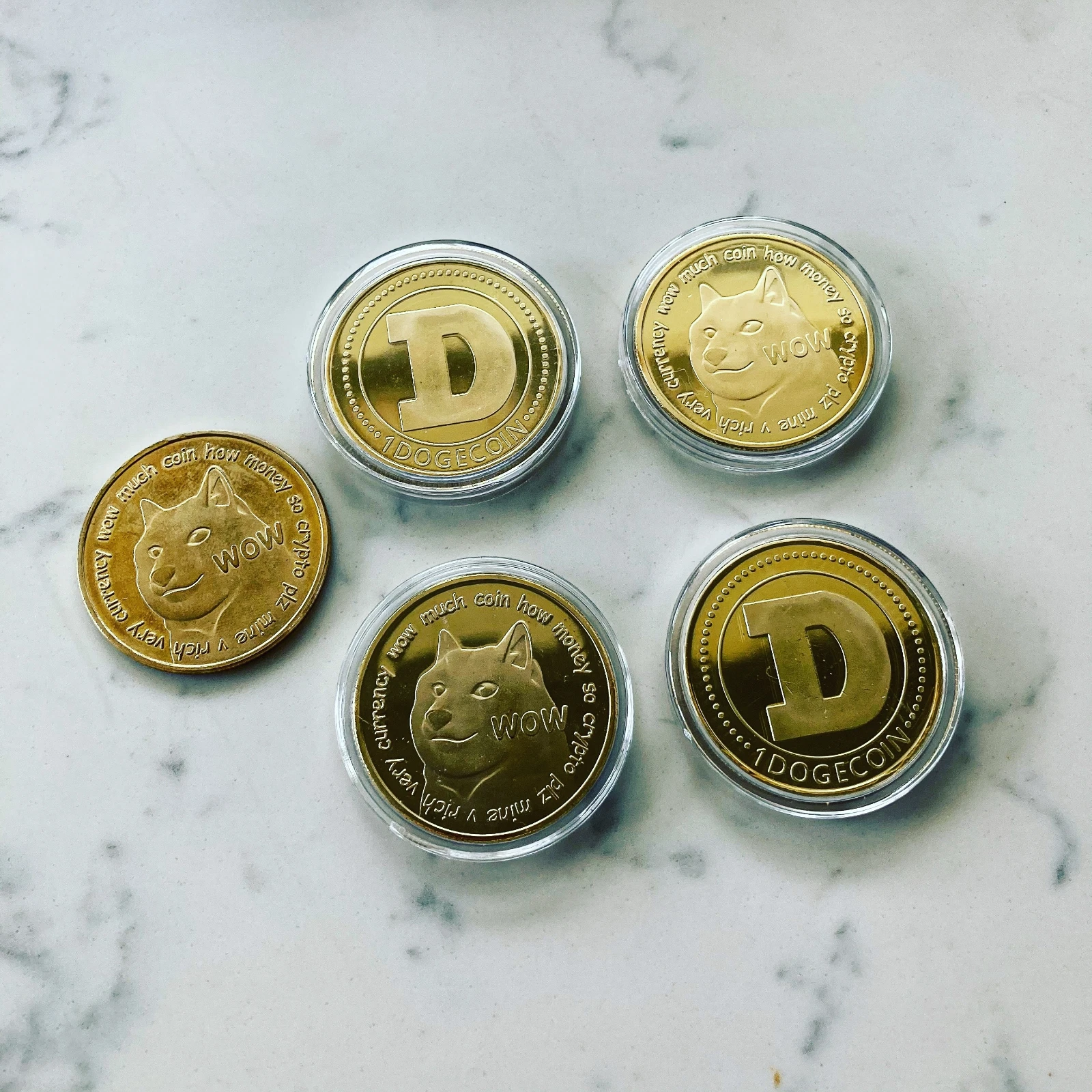 Five gold Dogecoin collectible coins on a white marble surface