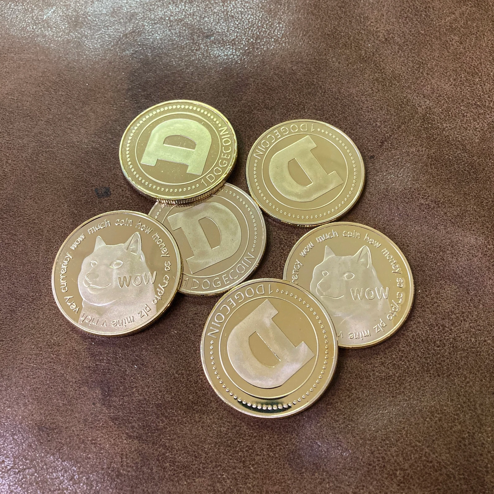 Six gold Dogecoin collectible coins fanned out on brown leather